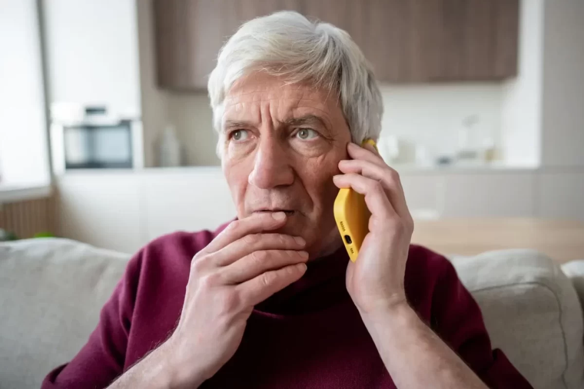 Starší muž, který drží mobilní telefon u ucha a vypadá znepokojeně.