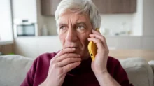 Starší muž, který drží mobilní telefon u ucha a vypadá znepokojeně.