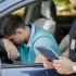 Policista komunikuje s řidičem sedícím v autě. Řidič má hlavu opřenou o volant a vypadá frustrovaně.