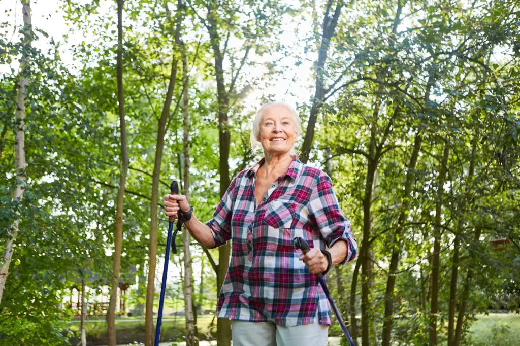 Starší žena při nordic walkingu uprostřed lesa. 