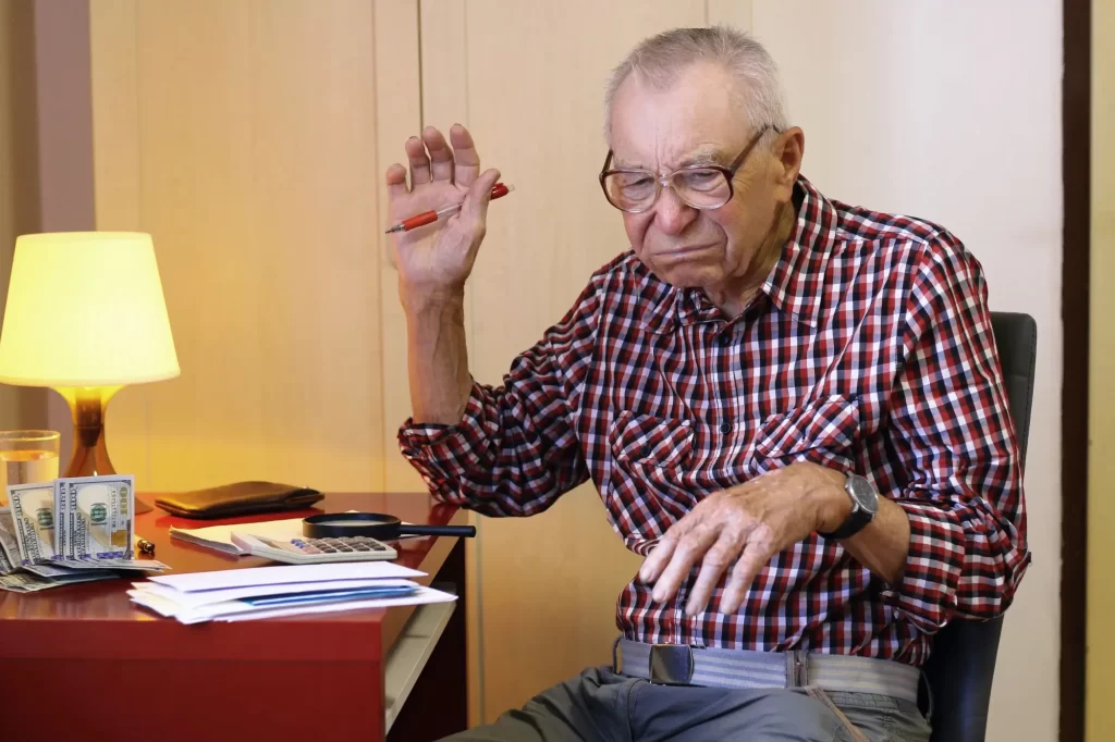sen2 - Techsvět Starší muž sedí u stolu s výrazem zklamání, v jedné ruce drží propisku, druhou zvedá v bezmocném gestu.