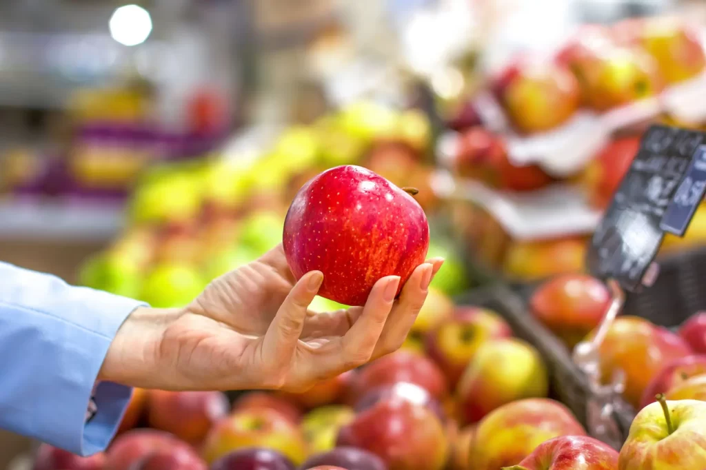 shutterstock_1348971797 - Techsvět detail na ženskou ruku v supermarketu, která drží lesklé jablko