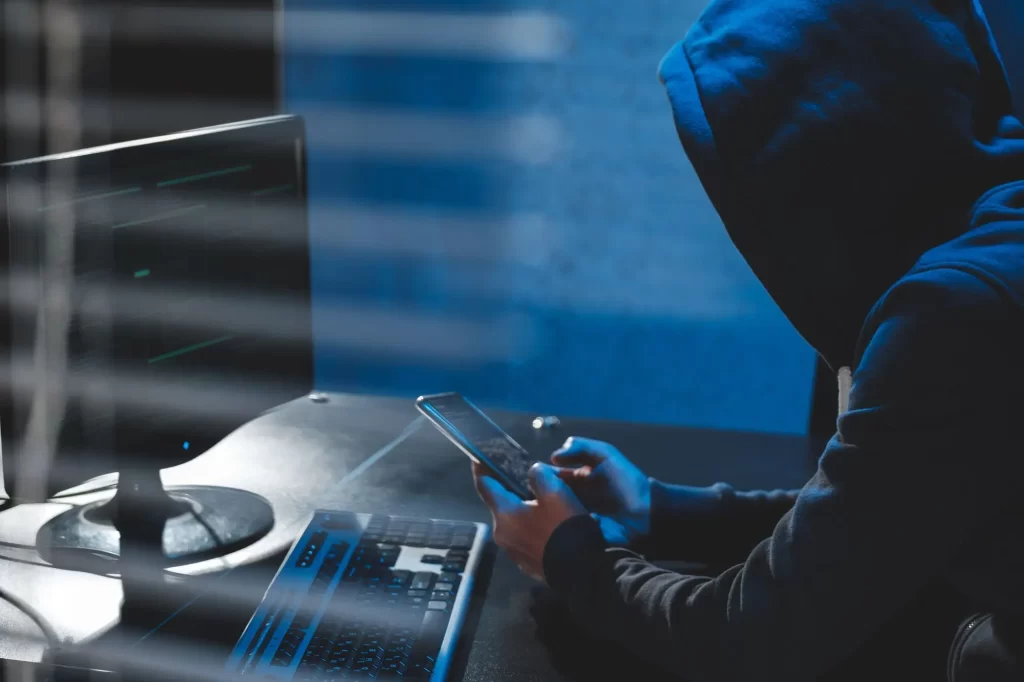 hacker v kapuci drží v ruce mobil