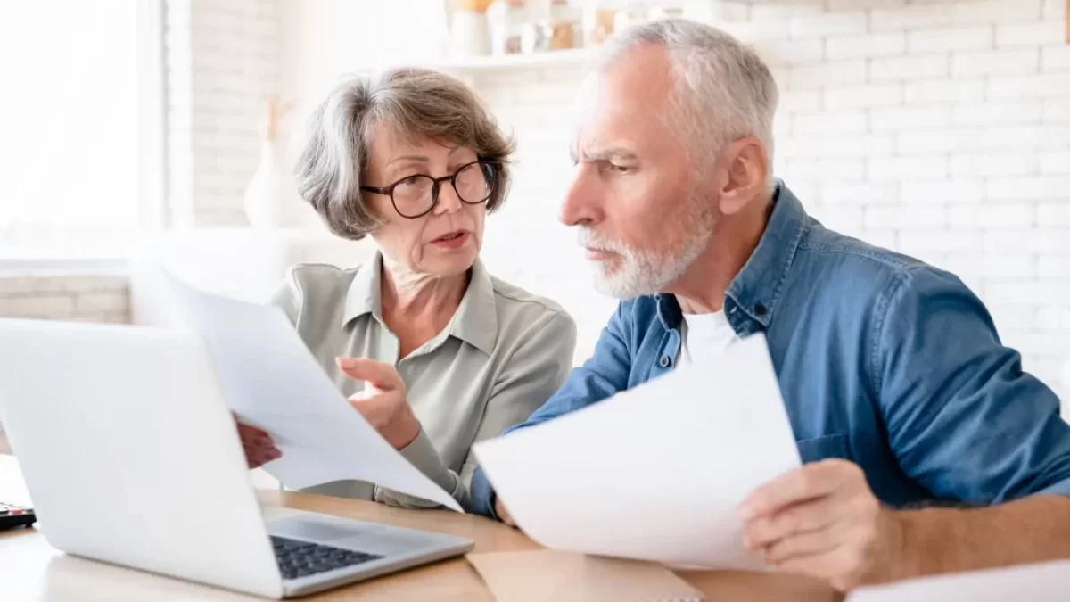 dvojice seniorů sedí u notebooku a prohlíží si papíry