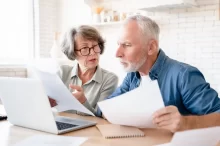 dvojice seniorů sedí u notebooku a prohlíží si papíry