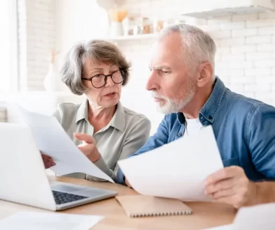 dvojice seniorů sedí u notebooku a prohlíží si papíry