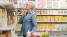 Starší žena stojící v obchodě u regálu s potravinami.