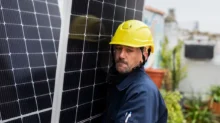 Muž ve žluté helmě nese solární panel