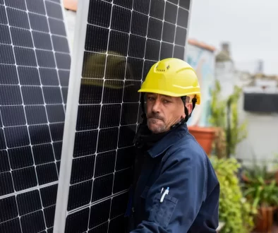 Muž ve žluté helmě nese solární panel