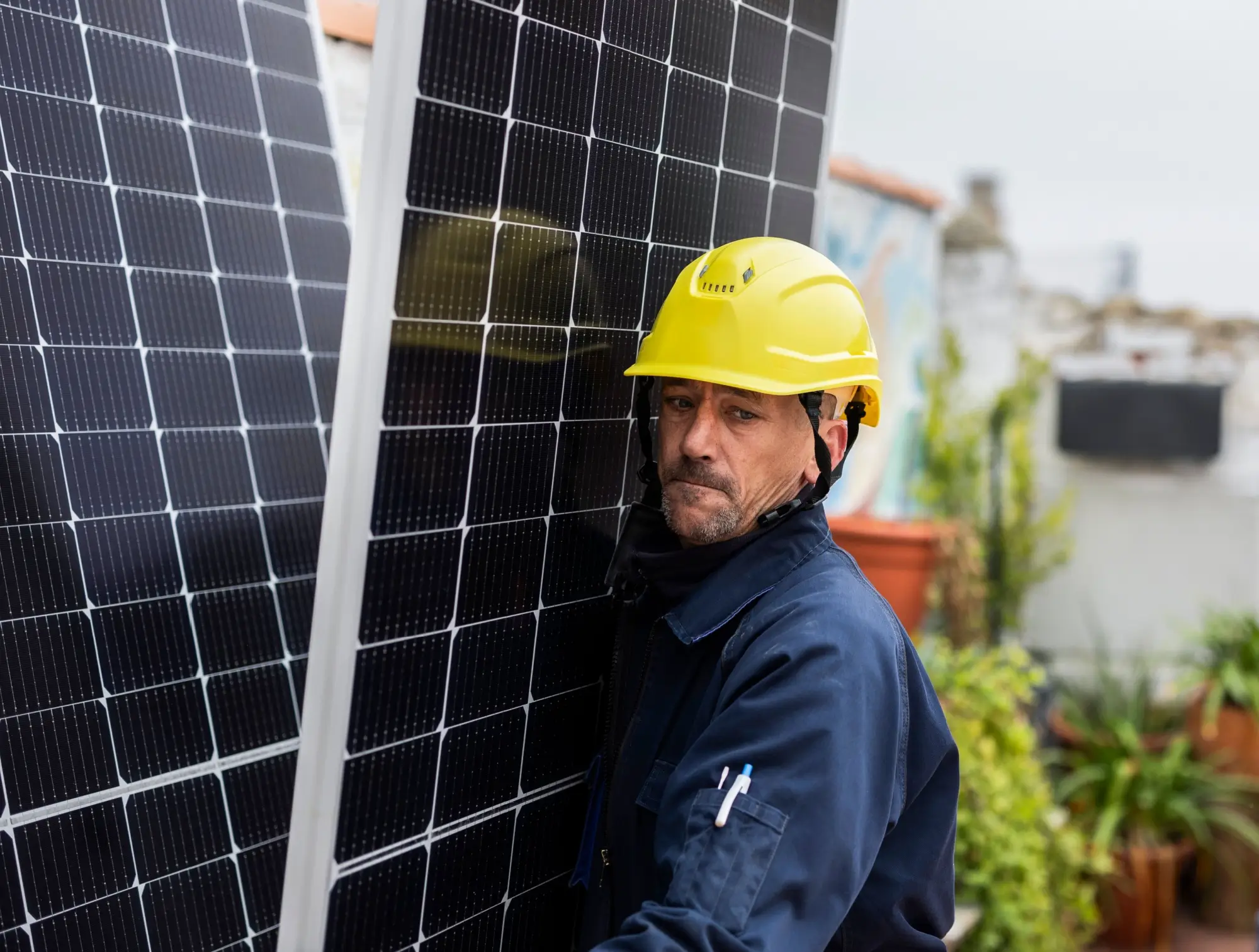 Muž ve žluté helmě nese solární panel