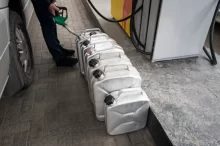 Muž na benzínce tankuje do několika plechových kanystrů