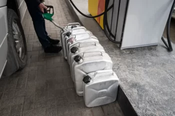 Muž na benzínce tankuje do několika plechových kanystrů