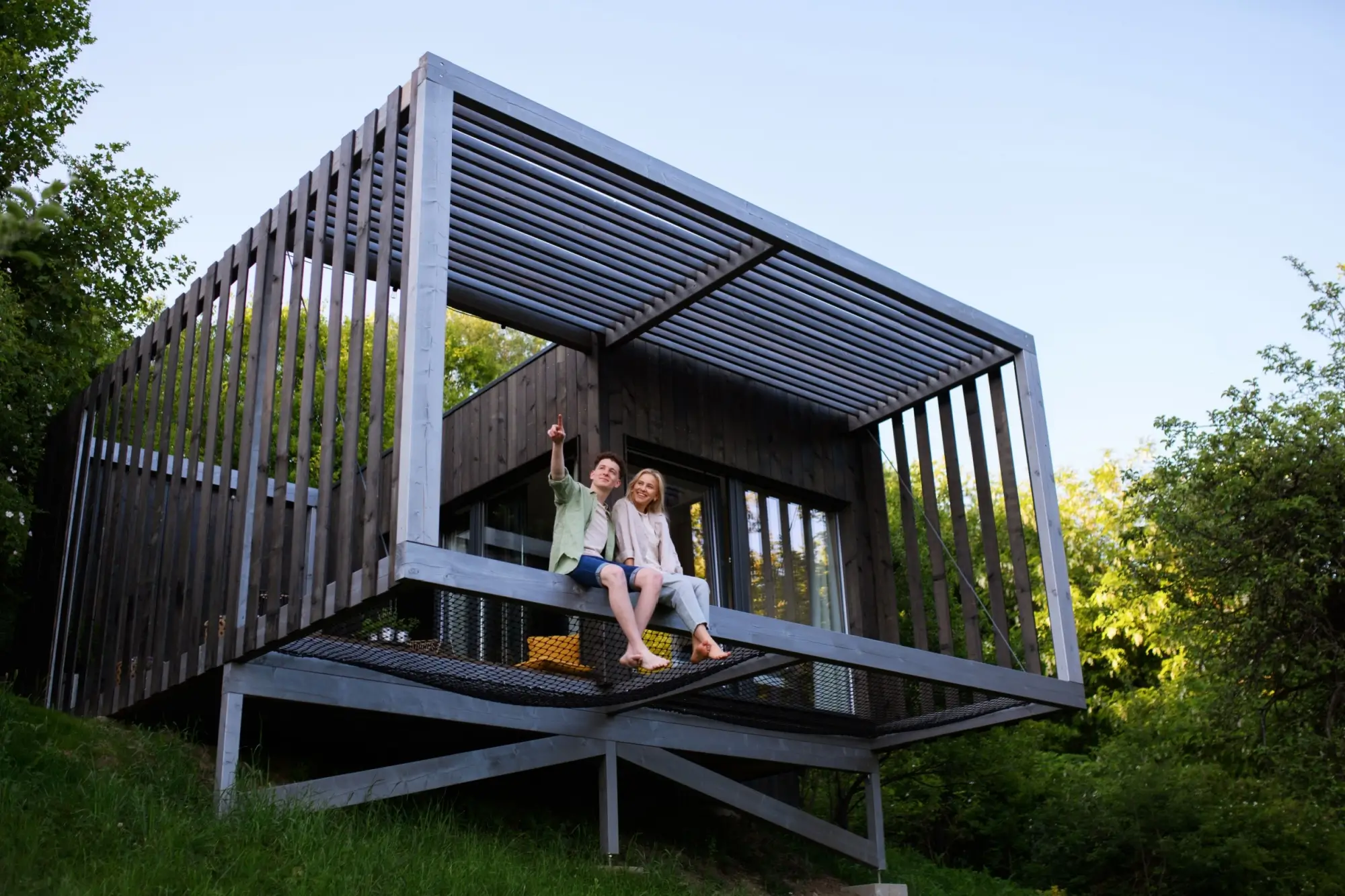 Moderní tiny house postavený na dřevěné konstrukci ve svahu, obklopený přírodou.