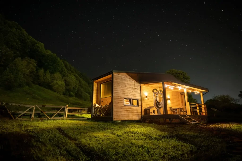 tiny2 - Techsvět Útulný tiny house ze dřeva osvětlený teplým světlem uprostřed noční krajiny.