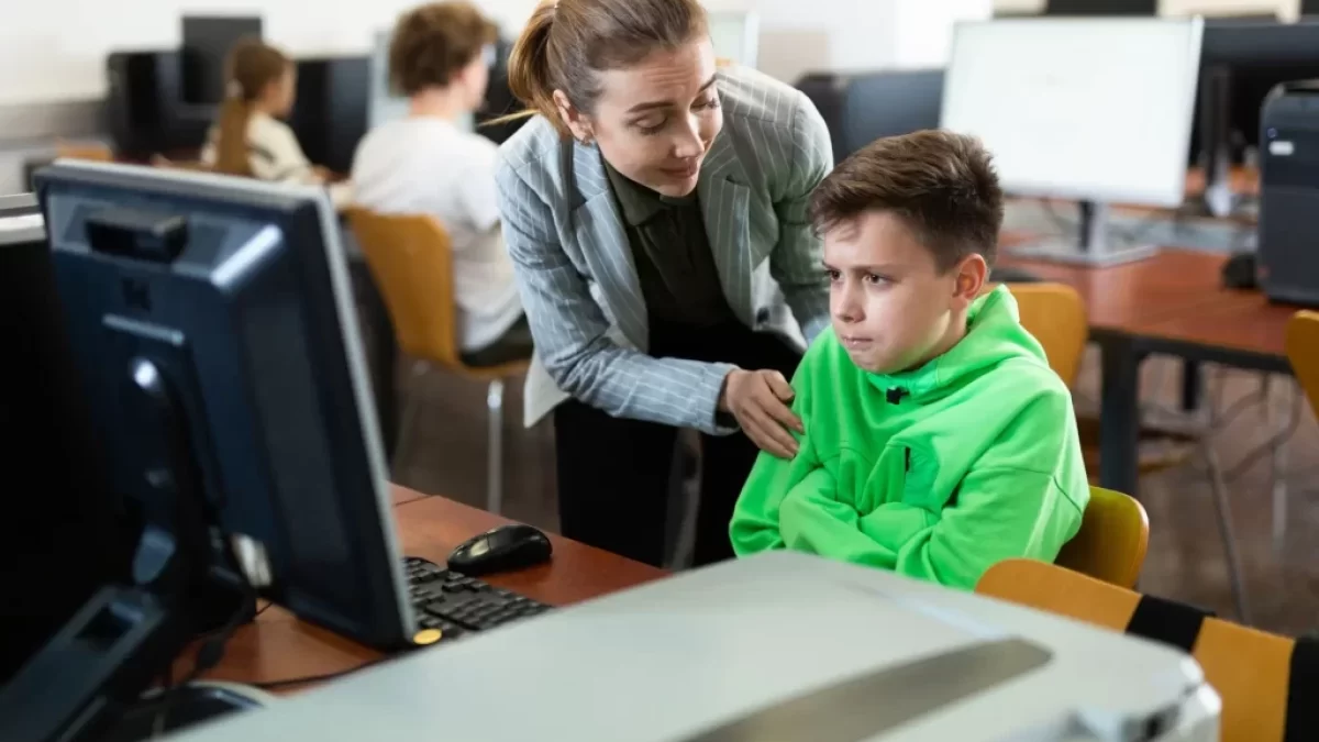 Učitelka utěšuje žáka v zelené mikině v učebně informatiky