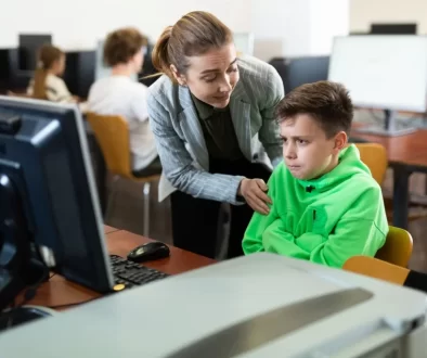 Učitelka utěšuje žáka v zelené mikině v učebně informatiky