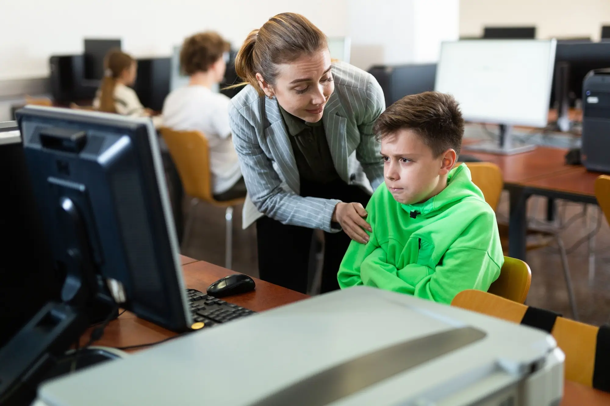 Učitelka utěšuje žáka v zelené mikině v učebně informatiky