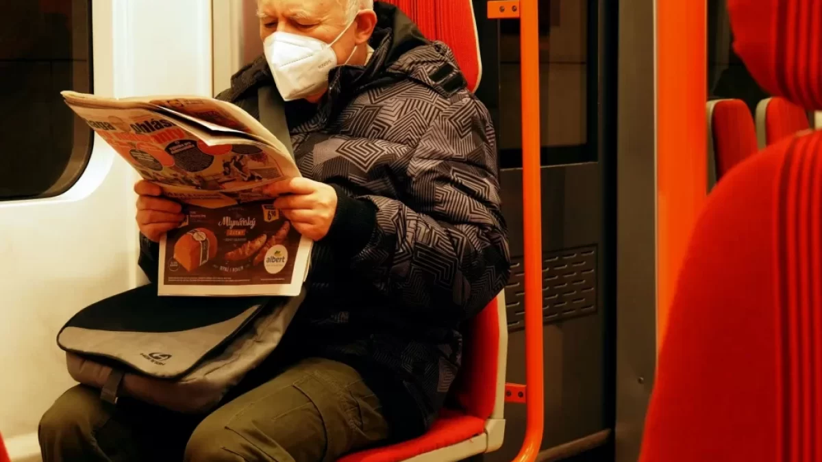 Starší muž v roušce si čte v metru noviny