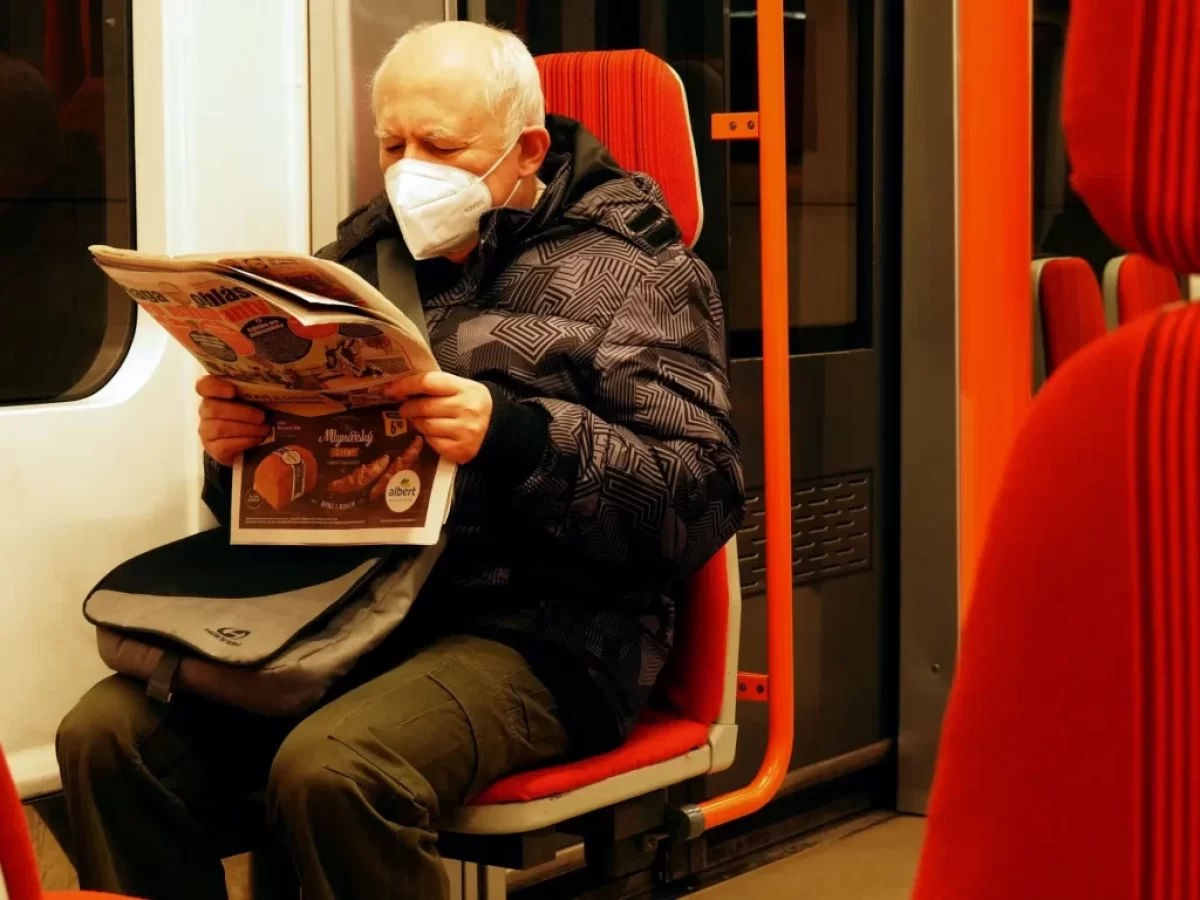 Starší muž v roušce si čte v metru noviny