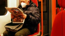 Starší muž v roušce si čte v metru noviny