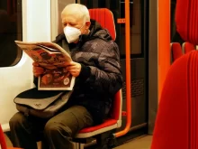 Starší muž v roušce si čte v metru noviny