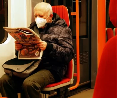 Starší muž v roušce si čte v metru noviny