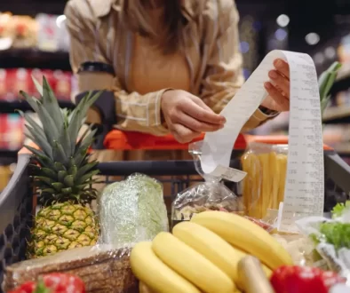 Žena v supermarketu, kontroluje dlouhý nákupní účet u plného vozíku s potravinami.