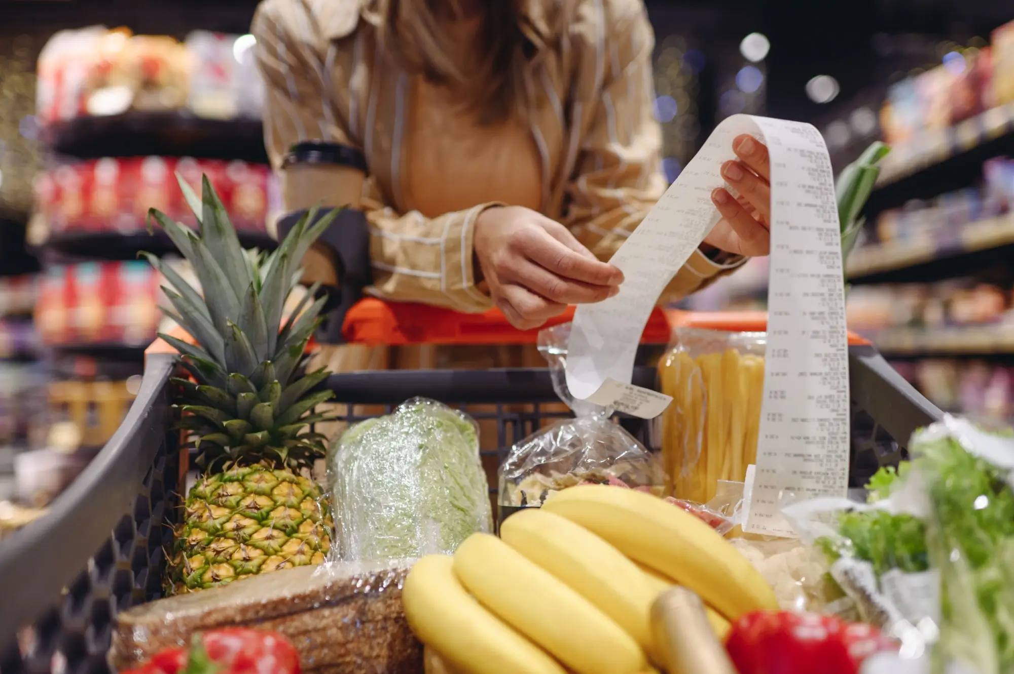 Žena v supermarketu, kontroluje dlouhý nákupní účet u plného vozíku s potravinami.