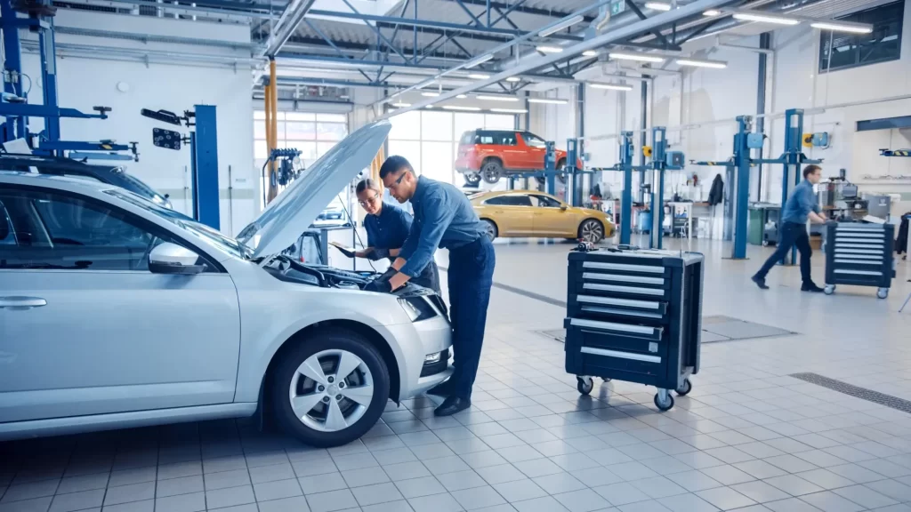 STK3 - Techsvět Moderní autoservis, kde dva technici – muž a žena – provádějí kontrolu stříbrného osobního auta s otevřenou kapotou.
