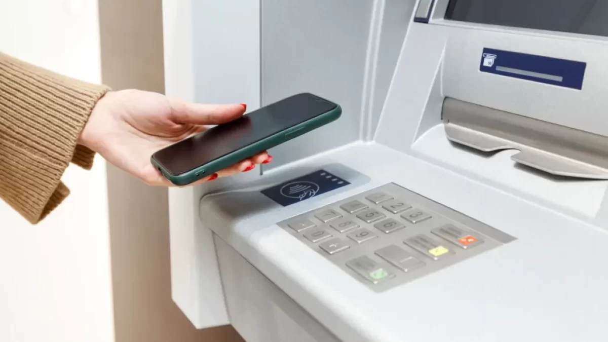 Žena přikládá telefon k bankomatu