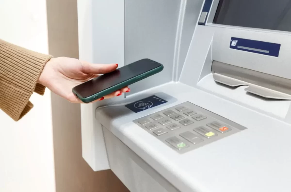 Žena přikládá telefon k bankomatu