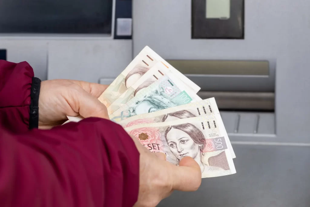 atm3 - Techsvět Detail rukou, které drží české bankovky v hodnotách 500, 200, 100 a 1 000 korun