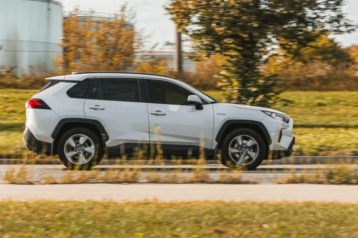 Bílá Toyota RAV4 v pohybu na silnici. Jde o SUV střední třídy s výraznými liniemi karoserie, černými ochrannými lemy blatníků.