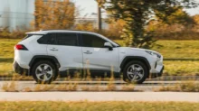 Bílá Toyota RAV4 v pohybu na silnici. Jde o SUV střední třídy s výraznými liniemi karoserie, černými ochrannými lemy blatníků.