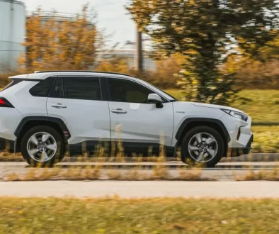 Bílá Toyota RAV4 v pohybu na silnici. Jde o SUV střední třídy s výraznými liniemi karoserie, černými ochrannými lemy blatníků.
