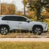 Bílá Toyota RAV4 v pohybu na silnici. Jde o SUV střední třídy s výraznými liniemi karoserie, černými ochrannými lemy blatníků.