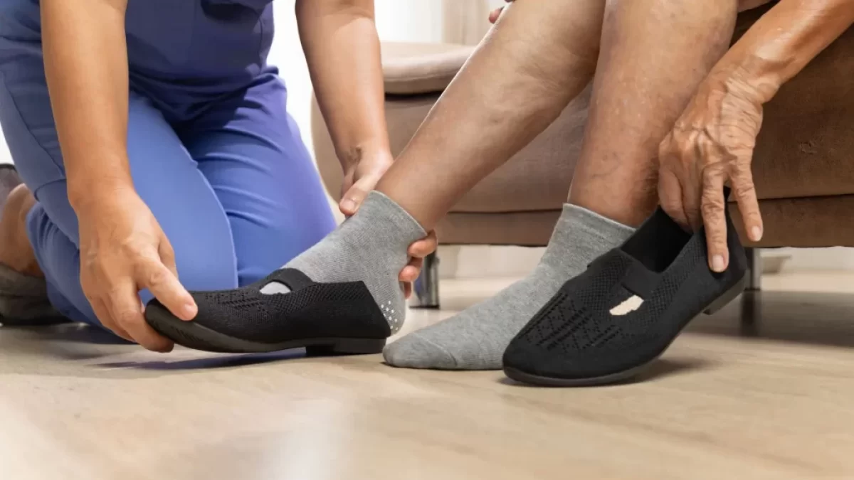 Seniorka, které pečující osoba pomáhá obout černou zdravotní obuv.