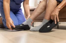 Seniorka, které pečující osoba pomáhá obout černou zdravotní obuv.