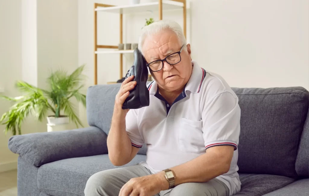 boty3 - Techsvět Starší muž na pohovce a drží si botu u ucha, jako by s ní telefonoval.