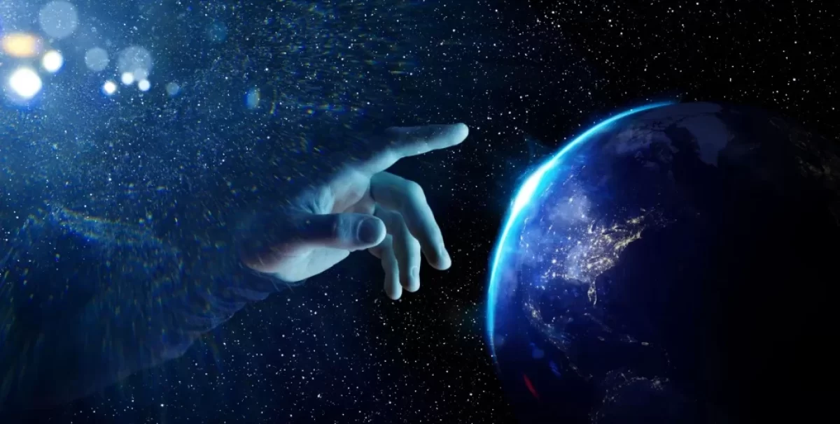 Vesmírná scéna ukazuje ruku, která se natahuje směrem k planetě Zemi, jako by ji právě dotvářela nebo uváděla do pohybu.