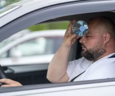 Muž sedí v autě s otevřenými okny a chladí se PET lahví s vodou