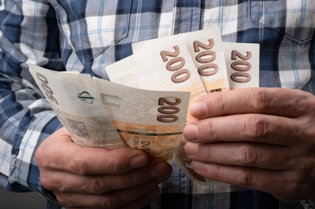 duch3 - Techsvět Muž v kostkované košili drží v rukou české bankovky.