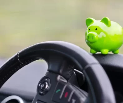 Interiér auta s detailem na volant a malou zelenou pokladničku ve tvaru prasátka, která stojí na palubní desce.