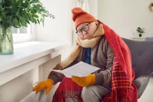 Starší muž sedí v kulichu a šále u topení