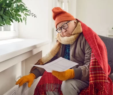 Starší muž sedí v kulichu a šále u topení