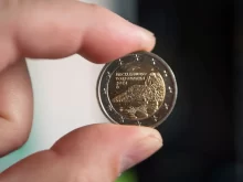 Detailní záběr na dvoueurovou minci, kterou muž drží mezi palcem a ukazováčkem.
