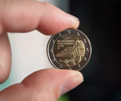 Detailní záběr na dvoueurovou minci, kterou muž drží mezi palcem a ukazováčkem.