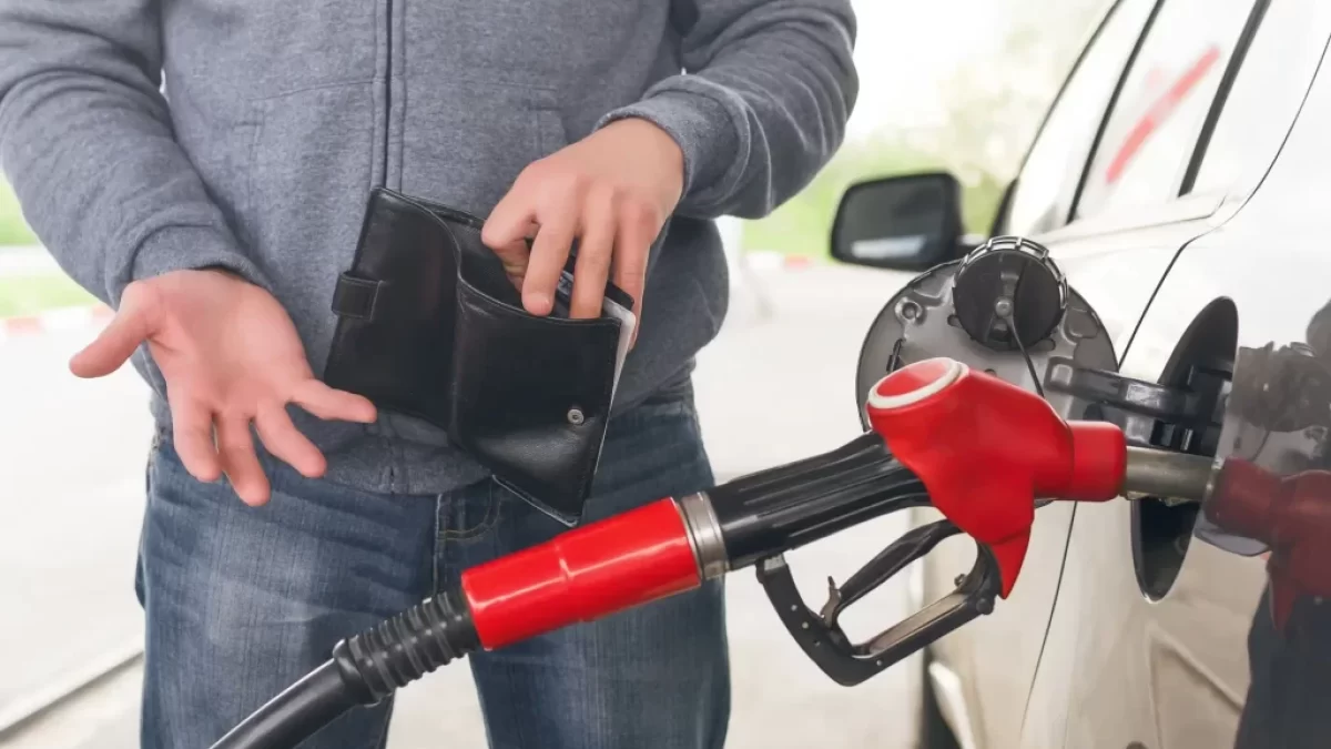 Muž u benzínové stanice tankuje a dívá se do prázdné peněženky