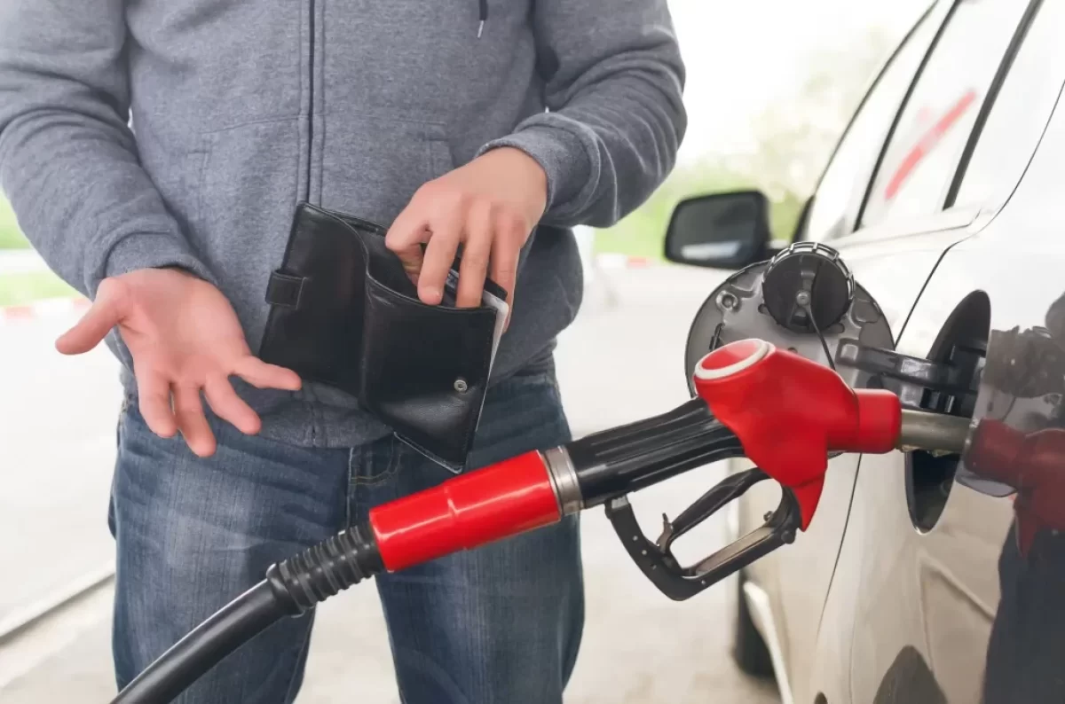 Muž u benzínové stanice tankuje a dívá se do prázdné peněženky