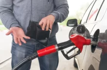 Muž u benzínové stanice tankuje a dívá se do prázdné peněženky